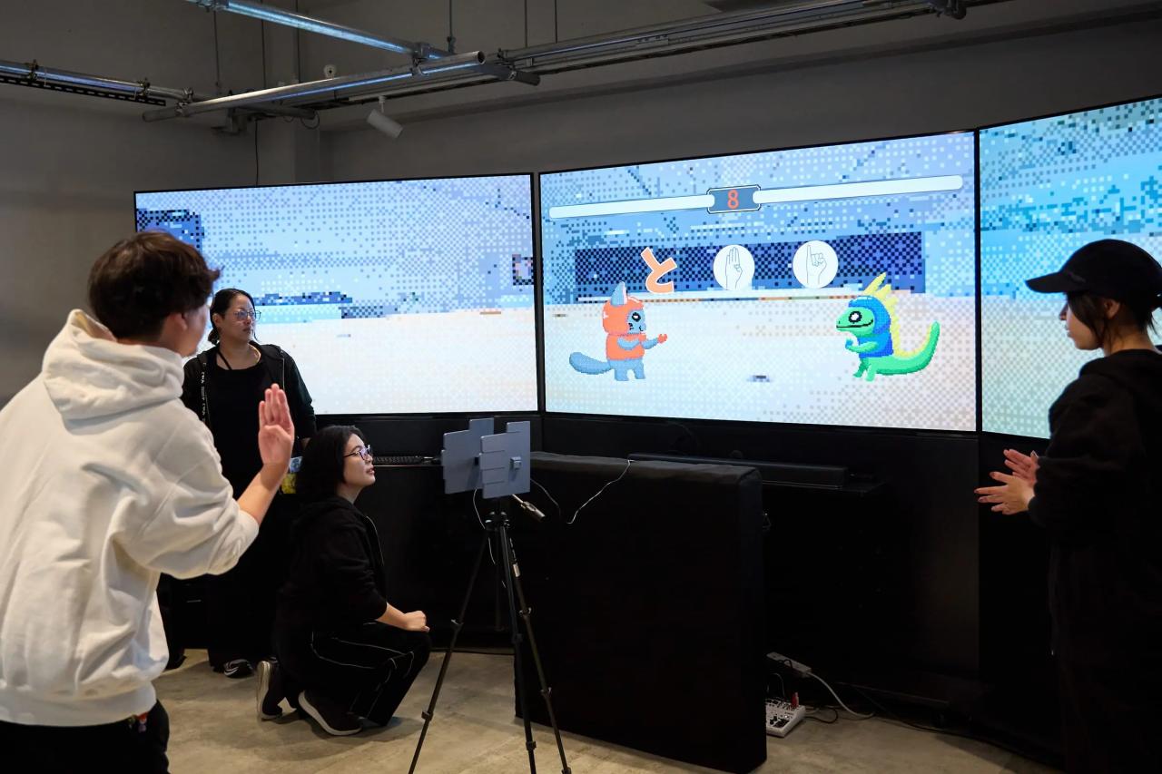 3面モニターの前で指文字を掲げるプレーヤー